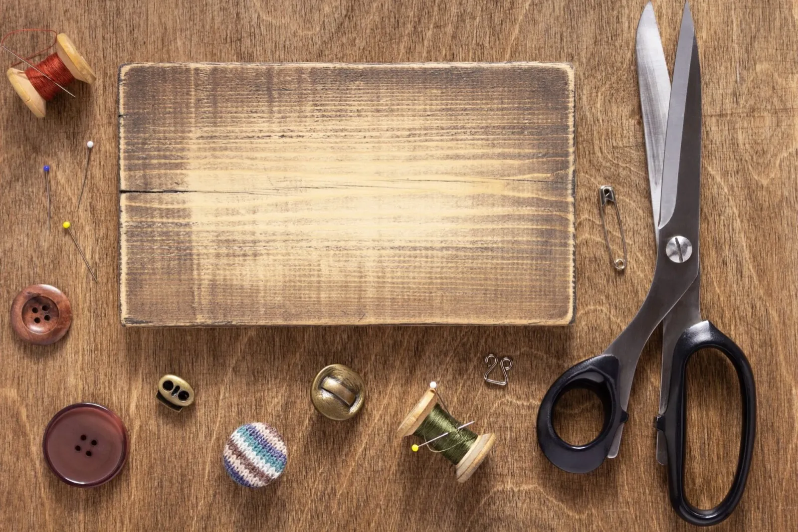 Tailor's scissors, thread spools, buttons and pins on a wooden work table